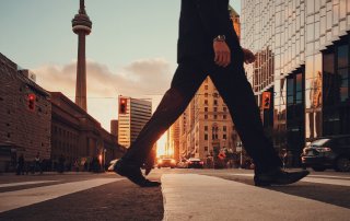 low angle shot of man crossing Toronto street with CN Tower visible in background