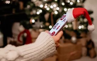 person shopping online on smartphone topped with santa hat with Christmas tree in background