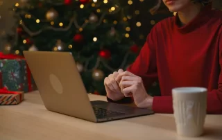 woman using laptop, sitting in front of Christmas tree