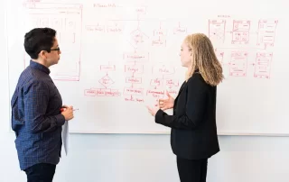 two colleagues discussing options in front of web design sketch on whiteboard