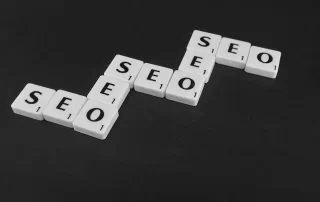 Scrabble tiles on black surface, spelling out “SEO” multiple times