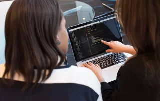 two web developers looking at code on laptop