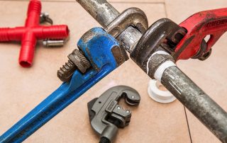 wrenches on pipe, with other plumbing tools and supplies in background