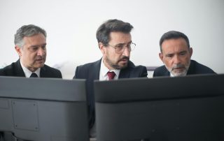 trio of colleagues in dark suits looking at dual-screen workstation