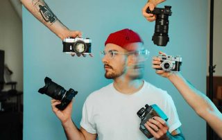 content creator concept image - man in white shirt and red hat surrounded by cameras held by multiple hands