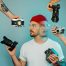 content creator concept image - man in white shirt and red hat surrounded by cameras held by multiple hands